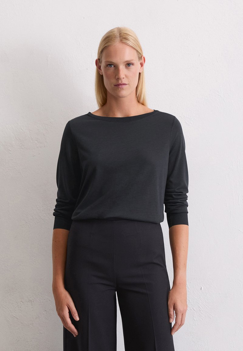 Zwart langemouwen shirt met een wijde halslijn en aansluitende mouwen, gemaakt van zachte stof. Gecombineerd met hoge taille zwarte broek.