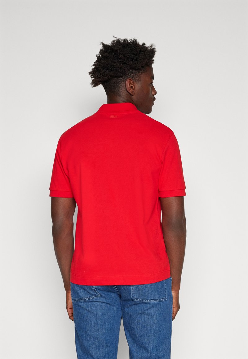 T-shirt polo rouge à manches courtes et col. Tissu simple et lisé, sans motifs ni dessins visibles. Ourlet ajustable à la taille.