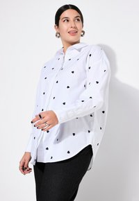 Witte button-up shirt met zwarte hartpatronen, lange mouwen en een licht gebogen hem. Bevat een klassieke kraag en een gladde stoftextuur.