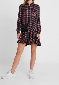 Långärmad skjortklänning i marinblå och röd rutigt med en utsvängd nederkant; matchad med vita sneakers och en liten svart crossbody-väska.