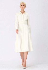 Robe chemise à manches longues, couleur crème, avec une taille ceinturée, présentant des rayures verticales et une jupe fluide jusqu'aux genoux. Texture lisse.