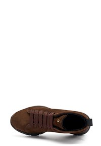 Zapatillas de ante marrón con punta redondeada, cordones marrones y suela de goma negra. Presenta un sutil acento de logo dorado en el lateral.