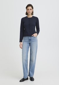 Cardigan bleu marine à manches longues avec un col rond et une fermeture à boutons. Jean bleu clair à jambes droites et chaussures noires. Design simple et près du corps.