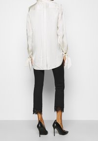 Crème satijnen blouse met strikmouwen, gecombineerd met zwarte slim fit broek met kanten zomen en zwarte stilettohakken.