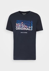 Námořnická modrá tričko s krátkým rukávem s nápisem "ORIGINALS" opakovaně v modro-bílé gradient textu a "JACK & JONES" pod ním.