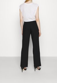 Černé široké kalhoty vyrobené z lehkého materiálu, s upraveným střihem a hladkou texturou. Spárované s vysokými podpatky.