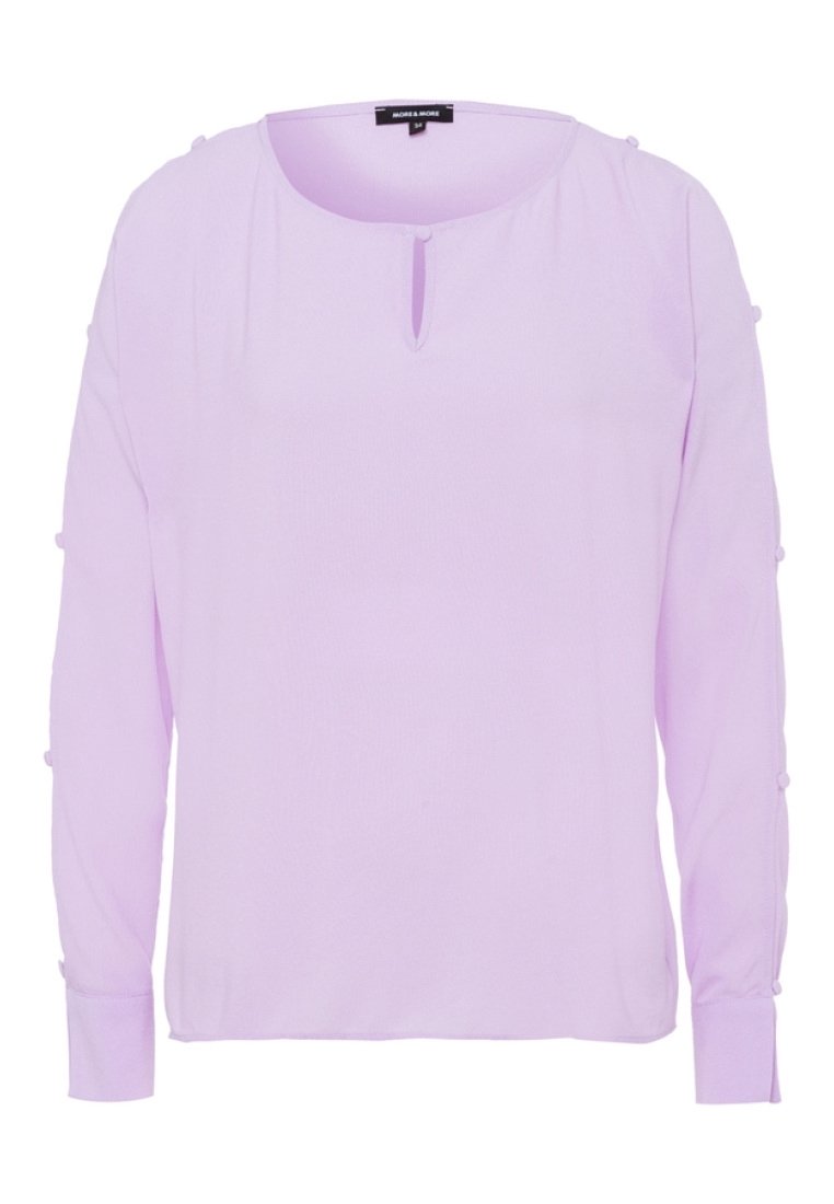 Blusa lunga a maniche con un collo rotondo e un dettaglio a chiave sul davanti di un leggero colore lavanda. Presenta particolari con bottoni sulle maniche. Tessuto liscio.