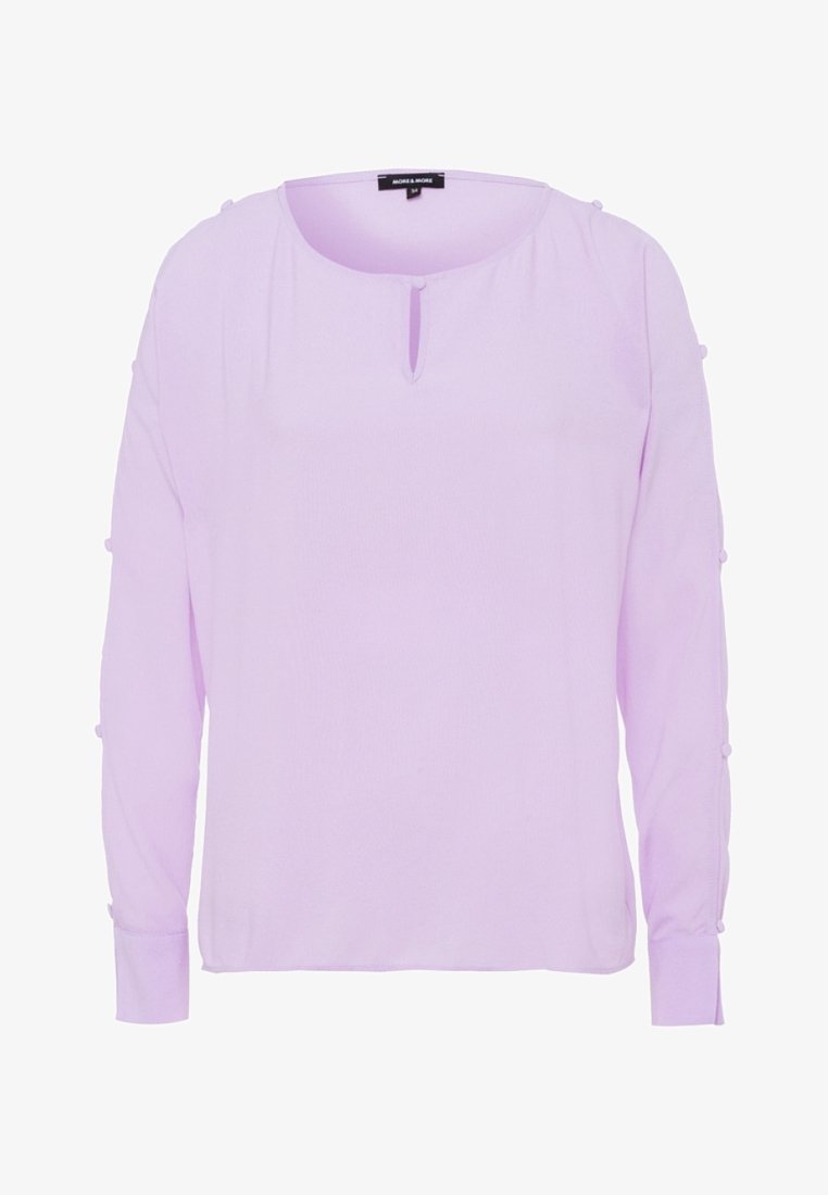 Blusa lunga a maniche con un collo rotondo e un dettaglio a chiave sul davanti di un leggero colore lavanda. Presenta particolari con bottoni sulle maniche. Tessuto liscio.