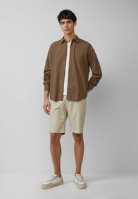 Bruin gestreepte overhemd met knopen, wit t-shirt eronder, beige short en lichte sneakers. Gladde textuur, casual pasvorm en neutrale kleuren.