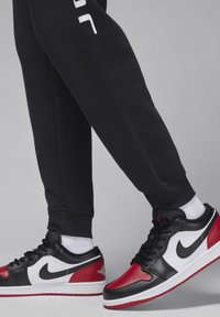 Nike Air Jordan tennarit mustana, punaisena ja valkoisena; matala malli, jossa on nahka materiaali, näkyvä Nike-swoosh ja teksturoituja yksityiskohtia.