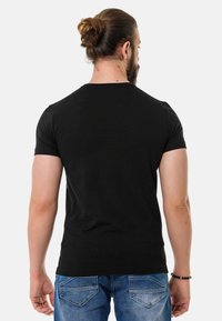 Schwarzes Kurzarm-T-Shirt von hinten betrachtet, mit Rundhalsausschnitt und slim fit, kombiniert mit blauen Jeans.