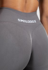 Szare legginsy o wysokim stanie, wykonane z teksturowanej tkaniny, z gładkim wykończeniem i markowym paskiem w talii z białym napisem "SMILODOX".