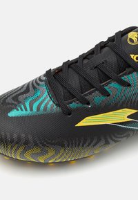 Taco de fútbol negro con acentos vibrantes en turquesa y amarillo, superficie texturizada y diseño estampado. Los cordones son negros, con tacos en la suela.