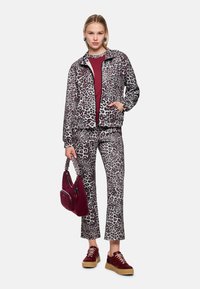 Leopardmuster-Jacke und Hose in Grau und Schwarz, kombiniert mit einem burgunderroten Oberteil und passender Handtasche, getragen mit weinroten Sneakers.