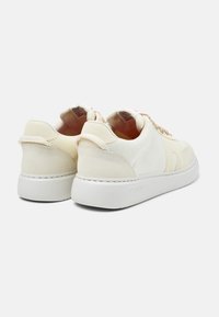 Cream-colored sneakers with suede and mesh accents, round toe, flat white sole, and minimalistic design. Features lace-up front and heel tab.