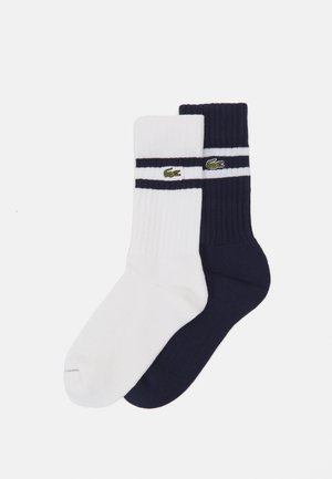 Cotton socks, one white and one navy, featuring ribbed texture and two horizontal stripes with embroidered green crocodile logo.