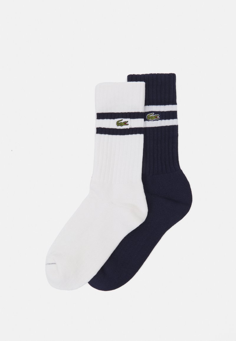 Calcetines de algodón, uno blanco y otro azul marino, con textura acanalada y dos rayas horizontales, decorados con el logo bordado de cocodrilo verde.