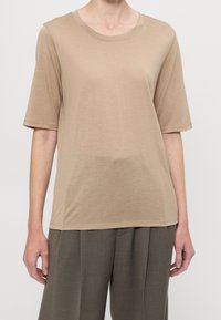 Beige tričko s krátkými rukávy a kulatým výstřihem, vyrobené z hladké, lehké tkaniny. Má volný střih a minimální švy.