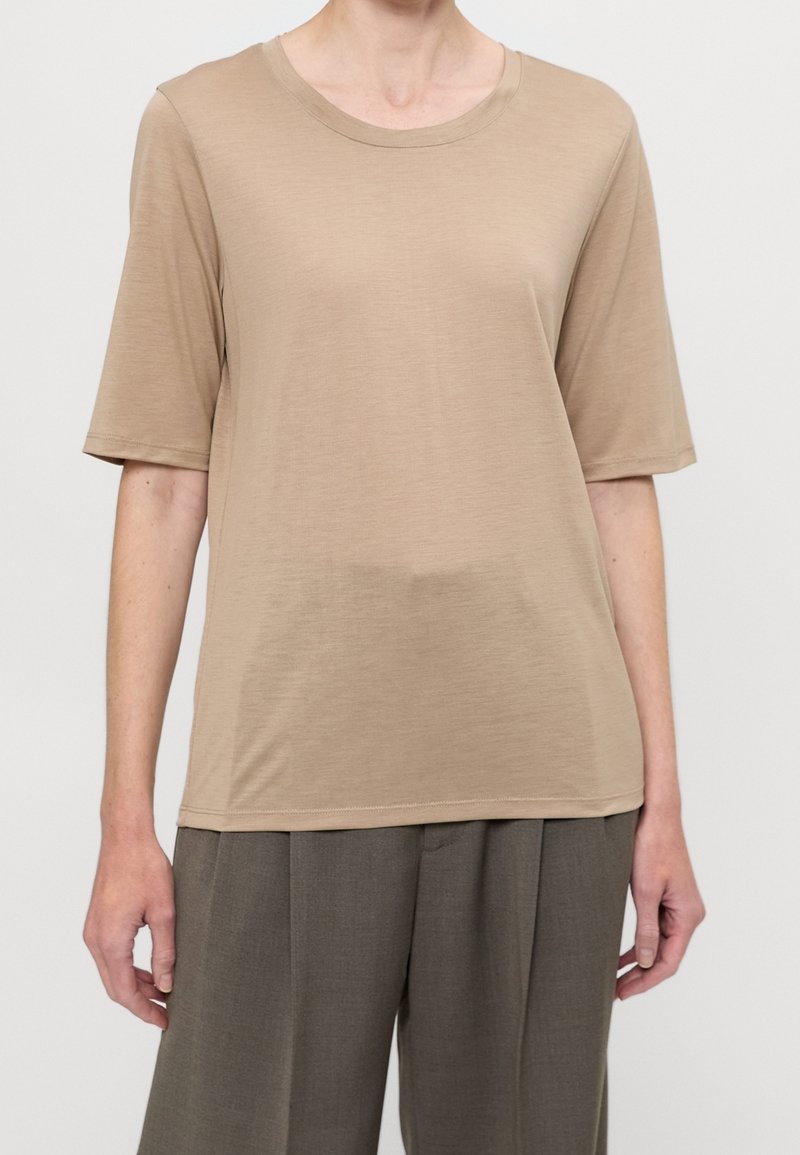 Beige tričko s krátkými rukávy a kulatým výstřihem, vyrobené z hladké, lehké tkaniny. Má volný střih a minimální švy.