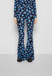 Pantalones de campana en una tela negra adornada con patrones florales azules y acentos rosas. Presentan una cintura ajustada y una textura suave.