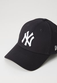 Black baseball cap made of cotton with a curved visor. Features a white embroidered NY logo on the front and ventilation eyelets on top.