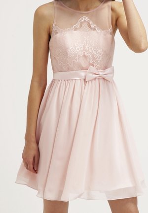 Robe rose clair sans manches avec corsage en dentelle, encolure transparente, ceinture en satin à la taille avec nœud, jupe évasée se terminant au-dessus des genoux.