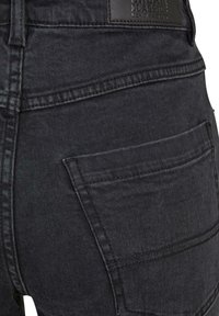 Jeans de mezclilla negra con una textura suave, que cuentan con bolsillos traseros y detalles de costura sutiles. Etiqueta de la marca visible en la cinturilla.