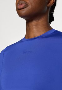 Mėlynas sportinis marškinėlis, pagamintas iš lygaus audinio, su apvaliu iškirpimu ir subtiliu iškilniu "BORG" logotipu ant krūtinės.