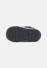 Navy blauwe kinderenschoen zool van getextureerd rubber, met een profielpatroon, luchtgaatjes en merklogo. Velcroband als accentdetail.