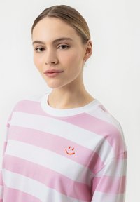 Roze en witte gestreepte blouse met lange mouwen en een ronde halslijn, met een kleine oranje glimlachende gezicht borduring op de borst.