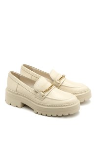 Beige leather loafers with a chunky sole, featuring a decorative gold chain across the instep and textured upper for added interest.