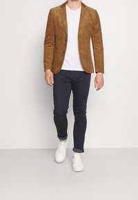 Hnědý kordový blazer, obtáhlý design, dvě přední kapsy, nošený přes bílé tričko, doplněný o námořnické kalhoty a bílé tenisky.