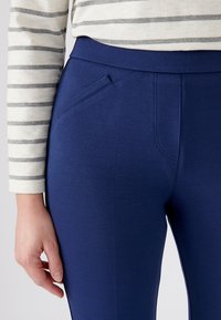 Marineblauwe elastische legging met een gladde textuur, voorzien van een klein voorvak en een hoge tailleband, gecombineerd met een gestreept langmouwshirt.