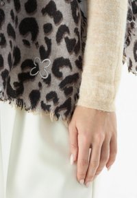 Sciarpa in stampa maculata con bordi sfrangiati, con un dettaglio di fiore ricamato grigio, abbinata a un maglione fitted beige chiaro.