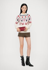 Knit sweater with multicolored patterns, paired with high-waisted brown shorts. Black ankle boots with gray socks. Holding a red clutch.