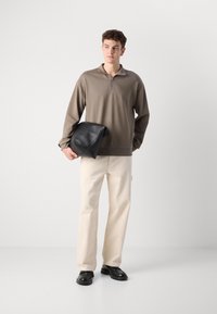 Barna, hosszú ujjú pulóver cipzáras gallérral, krém színű egyenes szabású nadrág, fekete cipők és oversize fekete clutches táska. Sima anyagok és minimális design.