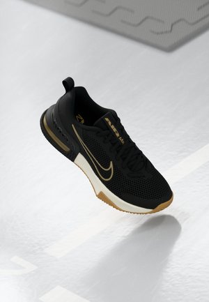 Schwarzer und goldener Nike Air Max Sportschuh mit Mesh-Obermaterial und Gummisohle, dargestellt, wie er über einer weißen strukturierten Oberfläche schwebt.