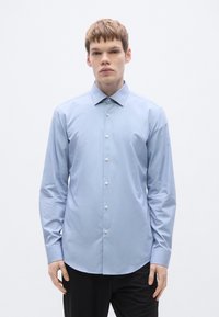 Helehallid särgipluus, mis on valmistatud siledast kangast, klassikalise krae ja nööpidega esiküljel. Lõige on keha järgi kohandatud, ümarate äärtega.