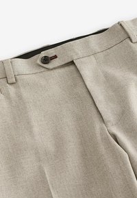 Pantaloni bej cu model herringbone, cu un front plat, închidere cu nasture și bucle pentru brâu. Țesătura are o textură netedă, cu un model subtil.