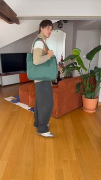 Groene gevoerde tas met bruine leren handvatten. Zachte textuur, rechthoekige vorm, ruime ontwerp. Binnenomgeving met planten en meubels.