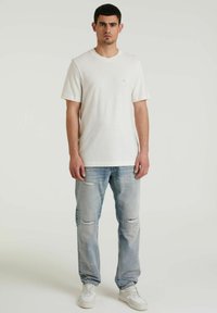 T-shirt bianco a maniche corte con scollatura rotonda. Indossato con jeans azzurri sfilacciati e sneaker bianche. Design semplice senza motivi.