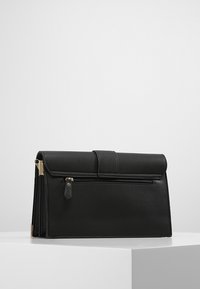 Sac à main en cuir noir avec un design structuré, comportant un rabat supérieur, des accessoires en métal doré et une poche zippée à l'avant pour un rangement sécurisé.