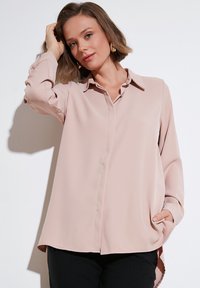 Light pink blouse made of smooth fabric, featuring a collared neckline, button-down front, and long sleeves with side pockets.