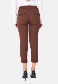 Pantaloni marroni a vita alta con un taglio su misura, dotati di tasche posteriori e risvolti, abbinati a scarpe con tacco alto nere.