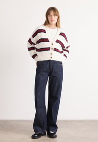 Cardigan a righe in crema, rosso e blu navy. Caratterizzato da un profondo scollo a V, sei bottoni e un tessuto lavorato. Abbinato a jeans a gamba larga blu scuro.