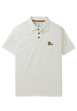 Polo blanc à manches courtes avec trois boutons noirs et un petit logo de botte jaune sur la poitrine gauche.