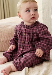 Combinaison bébé à carreaux bordeaux et noirs avec col à volants et boutons. Tissu doux avec poignets et chevilles élastiqués pour plus de confort.