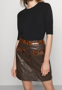 Svart stickad topp med korta ärmar, som är kombinerad med en brun läderkjol som har en orange ormmönstrad midja och dekorativa fickor.