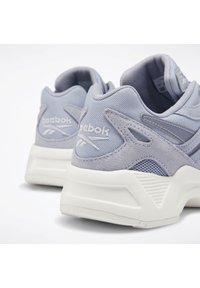Ljust grå Reebok-sneakers med ovandel i mesh och mocka, en dämpande vit mellansula och strukturerade detaljer på hälen för extra grepp och stil.