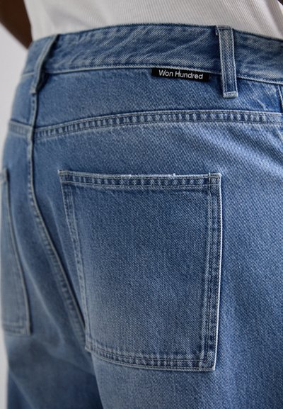 Jean en denim bleu clair avec une coupe standard, doté d'une poche arrière, de coutures visibles et d'une étiquette "Won Hundred" au niveau de la taille.